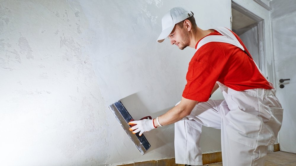 Een persoon brengt zorgvuldig renovlies van 150 gram per vierkante meter aan op een muur, terwijl behanglijm gelijkmatig wordt aangebracht voor een doe-het-zelf wandafwerking.
