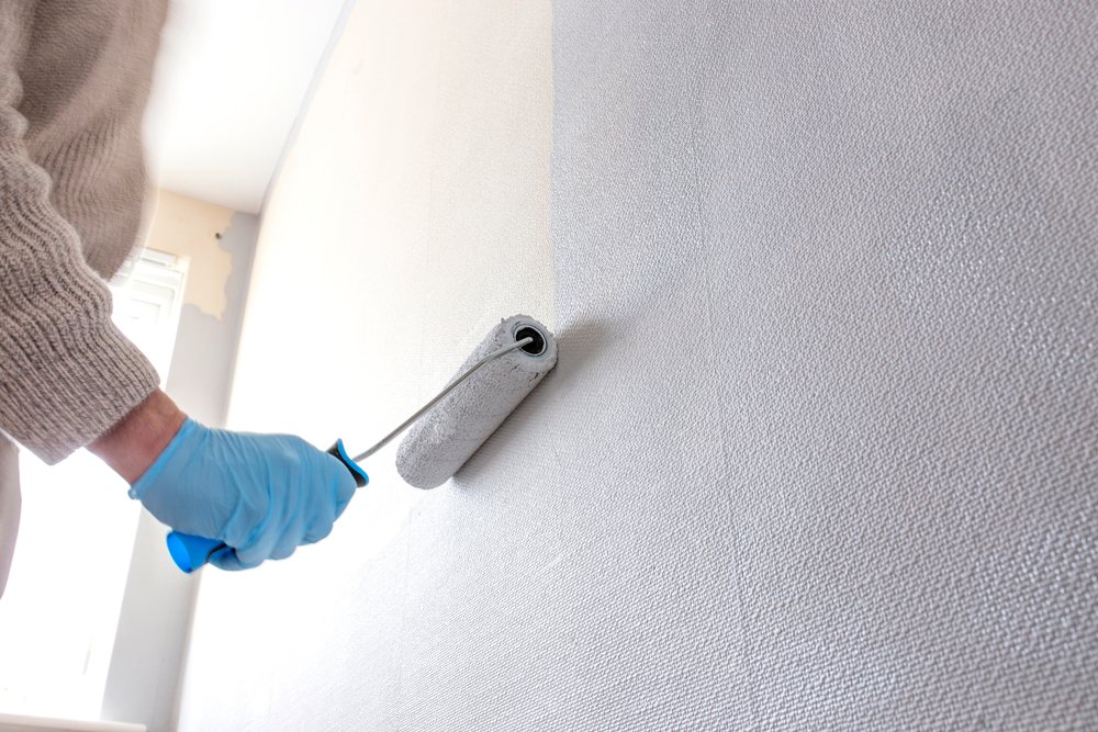 Een verfroller brengt verf aan op een muur bedekt met renovlies van 150 gram, terwijl een persoon de verf gelijkmatig verdeelt voor een professionele afwerking.